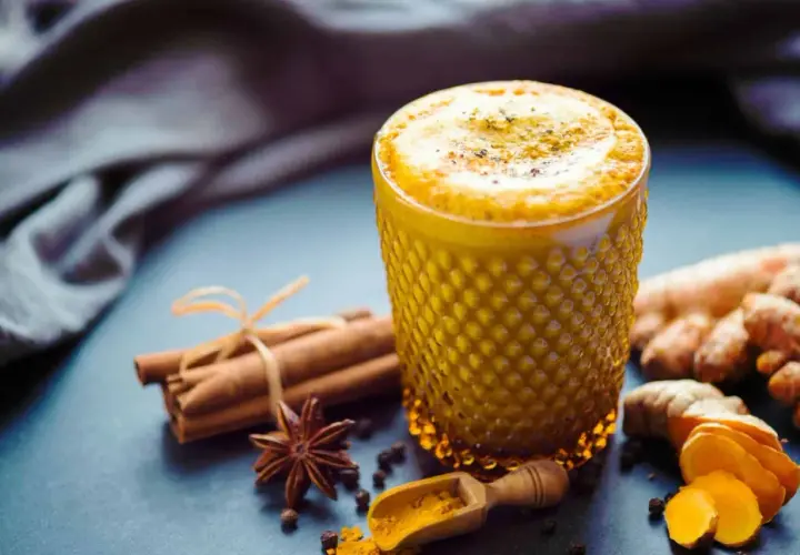 Ein Glas goldener Kurkuma Kaffee, verziert mit Zimtstangen, Sternanis und frischer Kurkuma.