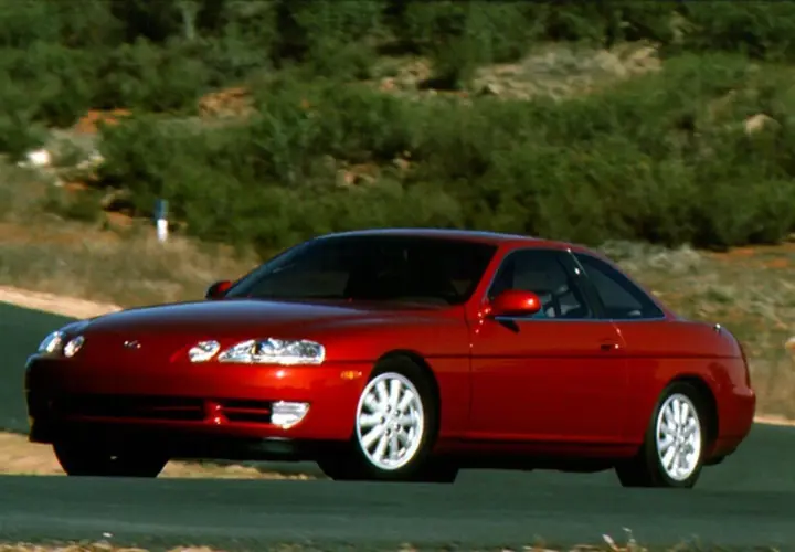 Czerwony Lexus SC400 na krętej drodze, otoczony zielonymi wzgórzami. Klasyczny sportowy samochód w ruchu.
