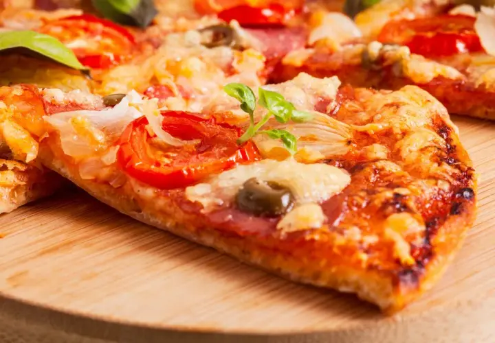 Pyszna pizza na serku wiejskim z pomidorami, oliwkami i bazylią, podana na drewnianej desce.