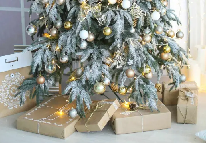 A frosted Christmas tree with gold and silver ornaments, fairy lights, and gifts wrapped in brown paper. Perfect christmas tree decor inspo for a cozy holiday.