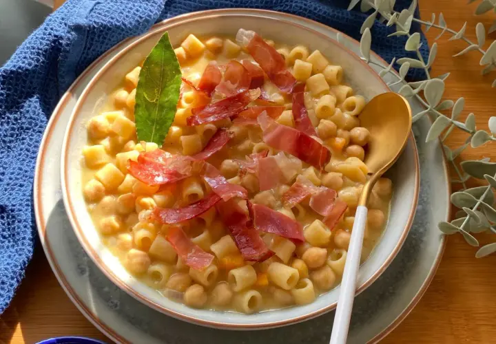 Un piatto fumante di pasta e ceci, arricchito da fette di prosciutto crudo e una foglia di alloro.