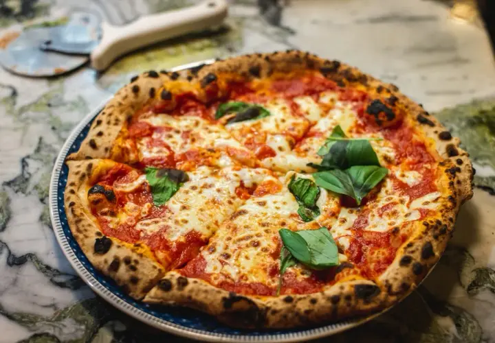 Pyszna pizza Margherita z bazylią na talerzu, obok nóż do pizzy.