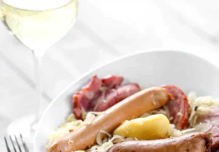 Un verre de vin blanc accompagne une choucroute de la mer généreuse avec saucisses et pommes de terre. Quel vin avec choucroute de la mer ?