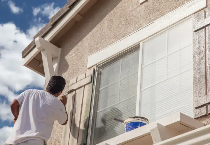 Pintor aplica pintura a persianas de ventana. ¿Cuál es la mejor pintura para fachadas? Busca durabilidad y resistencia a la intemperie.