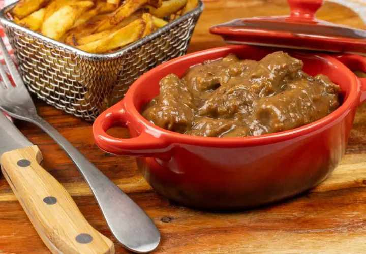 Un plat de carbonade flamande mijotée dans une cocotte rouge, accompagné de frites dorées dans un panier métallique. Un délice réconfortant.