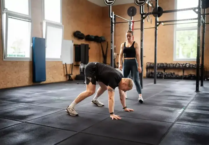 Trenerka obserwuje mężczyznę wykonującego burpee, ćwiczenie znane z intensywności.