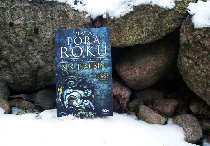 Książka "Piąta pora roku" N.K. Jemisin leży w śniegu między kamieniami. To opowieść o końcu świata, który przychodzi jak piąta pora roku.