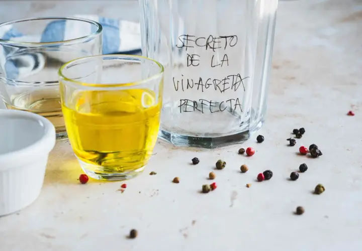 Ingredientes para la receta de vinagreta perfecta: aceite, vinagre y granos de pimienta.