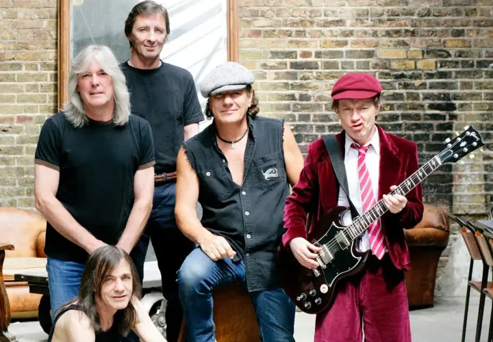 Zespół AC/DC w komplecie, gotowy do rock and rolla. Angus Young z gitarą, Brian Johnson w kultowym stroju.