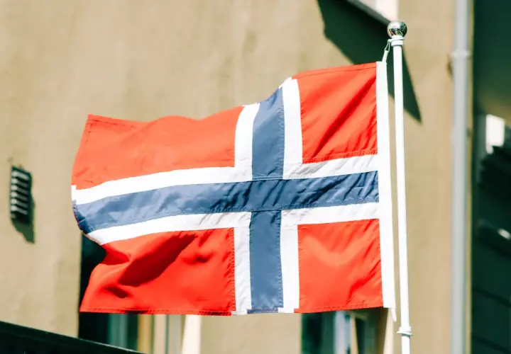 Flaga Norwegii powiewa na maszcie na tle budynku.