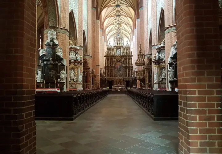 Wnętrze katedry w Pelplinie z rzędami ławek i bogato zdobionym ołtarzem głównym.