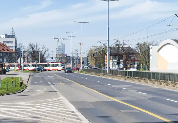 Ulica z tramwajem, samochodami i budynkami w tle.