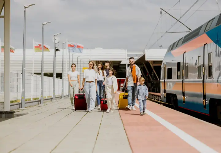 Rodzina z walizkami na peronie, obok pociągu. Planujesz podróż? Sprawdź, jak dojechać do Lublina!