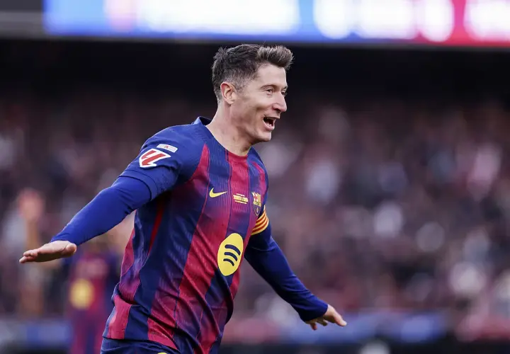 Piłkarz Robert Lewandowski w koszulce FC Barcelony świętuje bramkę na tle trybun.