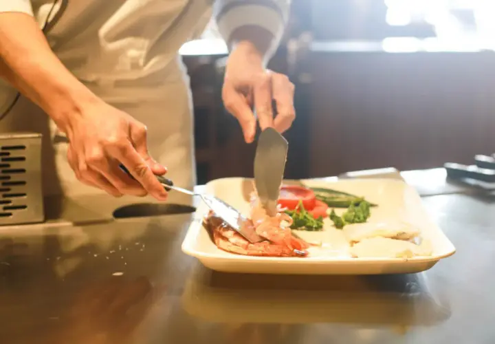 Kucharz przygotowuje danie z krewetek i warzyw, ćwicząc umiejętności do egzaminu zawodowego gastronomia.