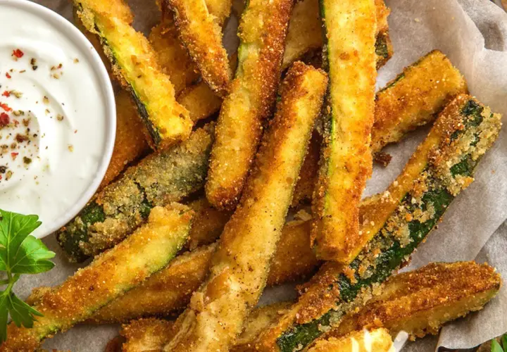 Bastoncini croccanti di zucchine in friggitrice ad aria, dorati e invitanti, serviti con una salsa cremosa.