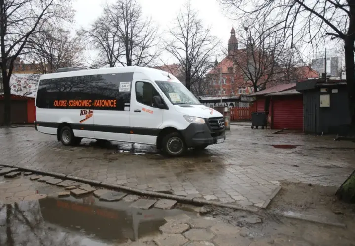 Biały bus Kik-Bus z napisem "OLKUSZ-SOSNOWIEC-KATOWICE" na mokrym placu przed budynkiem dworca.