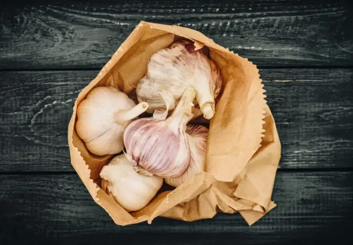 Frische Knoblauchzehen in einer Papiertüte, bereit zum **knoblauch lagern** auf dunklem Holz.
