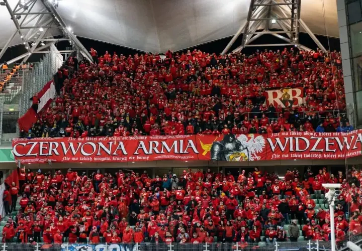 Tłum kibiców Widzewa w czerwonych barwach, z transparentem "Czerwona Armia Widzewa".