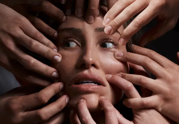 Volto di donna circondato da mani che la stringono, espressione di disagio, forse un simbolo del disturbo schizoide di personalità.