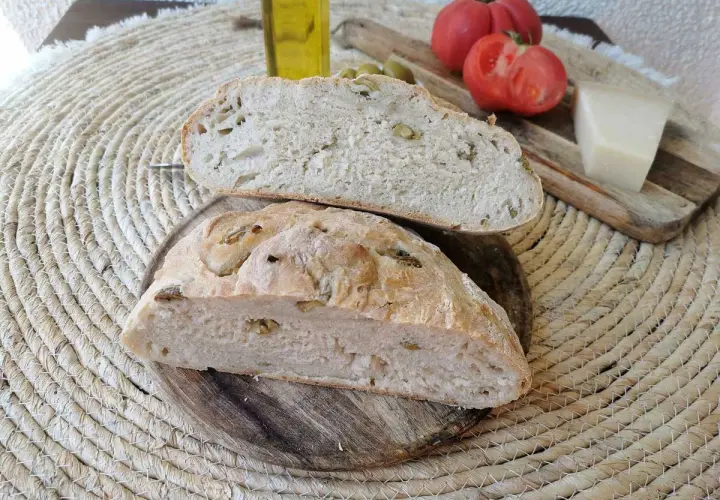 Pan rústico con aceitunas, tomates, queso y aceite de oliva. Un delicioso pan de aceitunas listo para disfrutar.