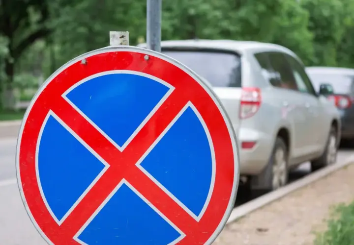 Znak zakazu zatrzymywania się b36. Samochody stoją w rzędzie przy ulicy, ale ten znak przypomina, że nie wolno tu parkować.