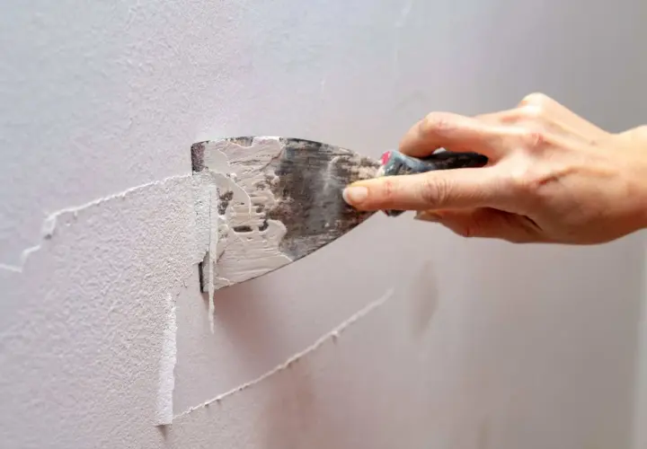 Mano usa una spatola per rimuovere la pittura lavabile dal muro, un passo fondamentale per preparare la parete a una nuova tinteggiatura.