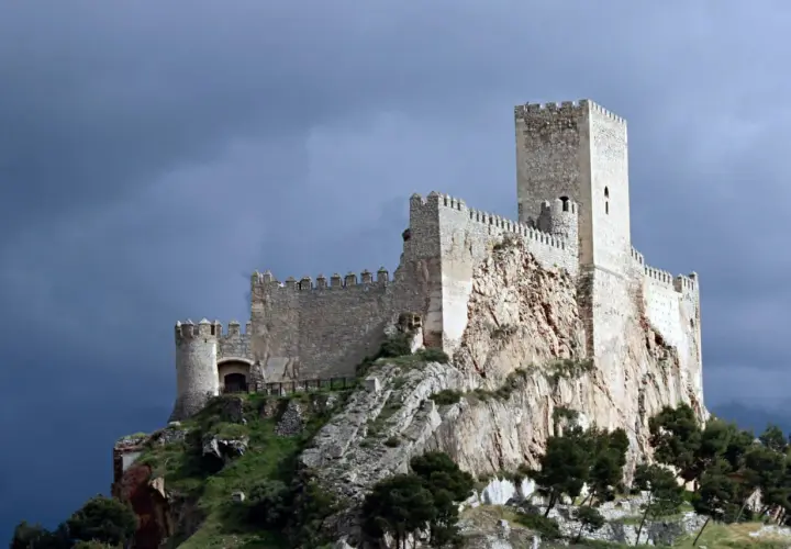 Castillo medieval en lo alto de un peñasco, parte de la ruta de la lana, bajo un cielo tormentoso.