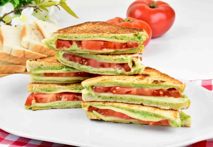 Pyszne włoskie kanapki z serem, pomidorami i zielonym pesto, ułożone na talerzu.