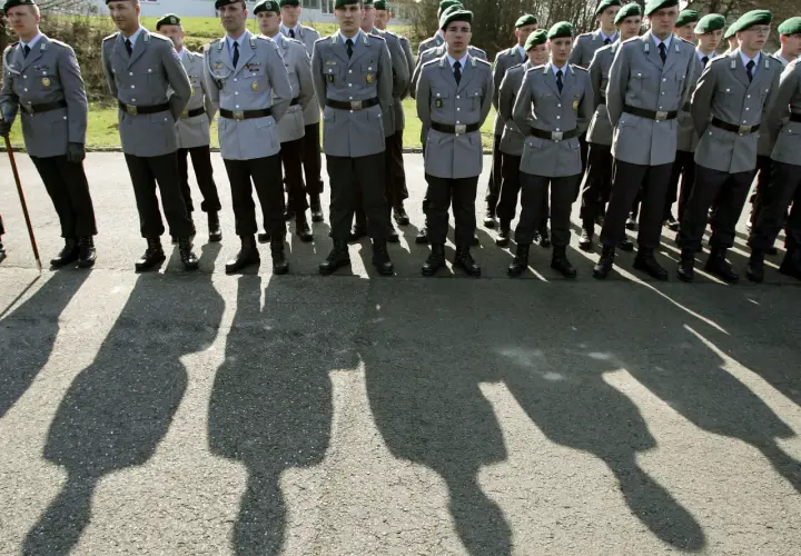 Soldaten der Bundeswehr in Uniform mit grünen Baretts stehen Spalier. Ihre Schatten werfen lange Linien auf den Asphalt.