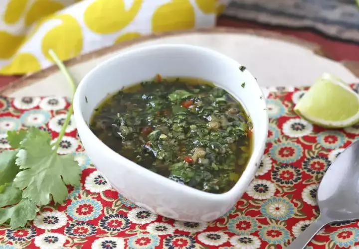 Aromaticzny sos chimichurri w białej miseczce, obok ćwiartka limonki i świeża kolendra.