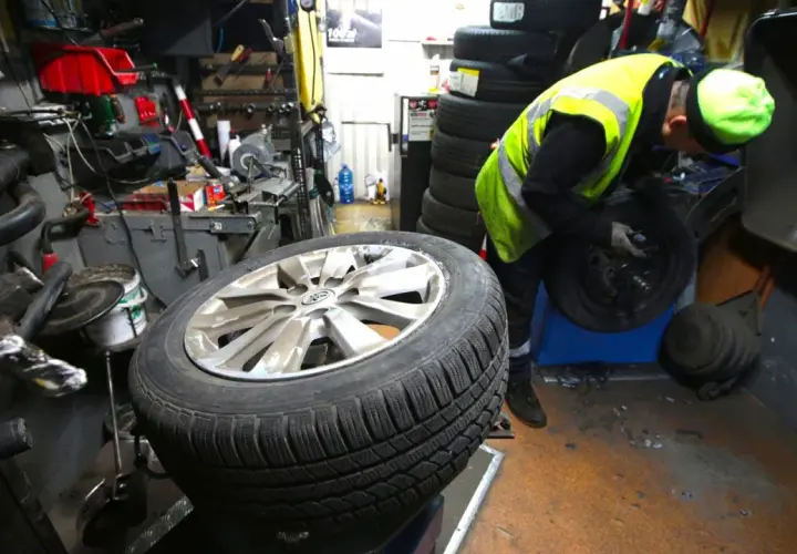 Mechanik w kamizelce odblaskowej pracuje przy kole. Słychać buczenie opon podczas jazdy, gdy pracownik wymienia oponę.
