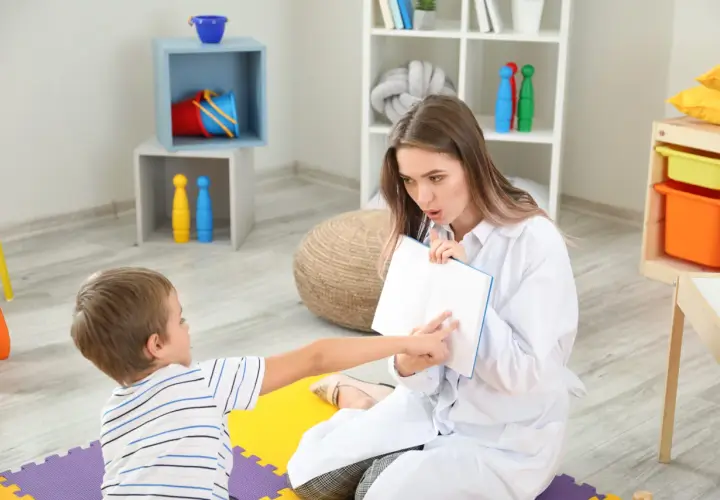 Terapia logopedyczna dla dziecka z zacinaniem się podczas mówienia u dorosłych. Terapeuta pokazuje dziecku książkę.
