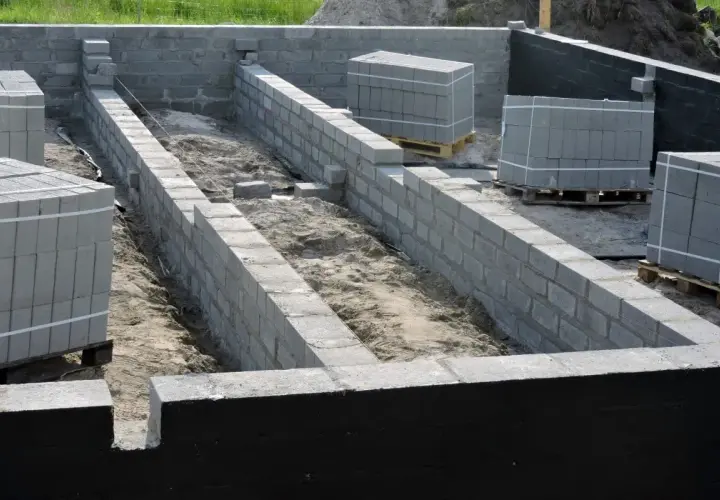 Budowa fundamentów: jak połączyć stary fundament z nowym. Ściany z bloczków betonowych, materiały budowlane na paletach.