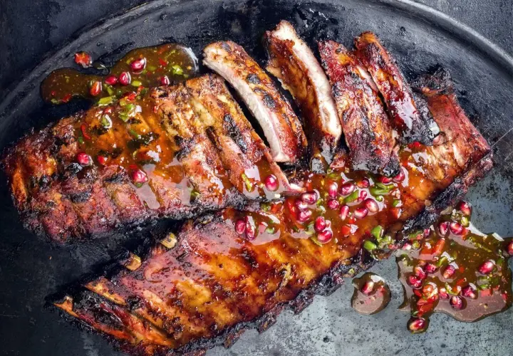 Soczyste żeberka w marynacie, polane aromatycznym sosem z granatem i chili, podane na metalowej tacy.