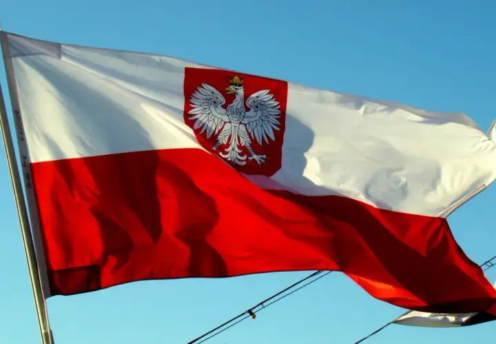 Polska flaga na statku powiewa na wietrze na tle błękitnego nieba. Biało-czerwona flaga z orłem w koronie dumnie reprezentuje kraj.