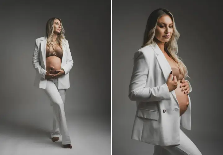 Elegancka sesja ciążowa w studio. Przyszła mama w białym garniturze czule obejmuje brzuszek.