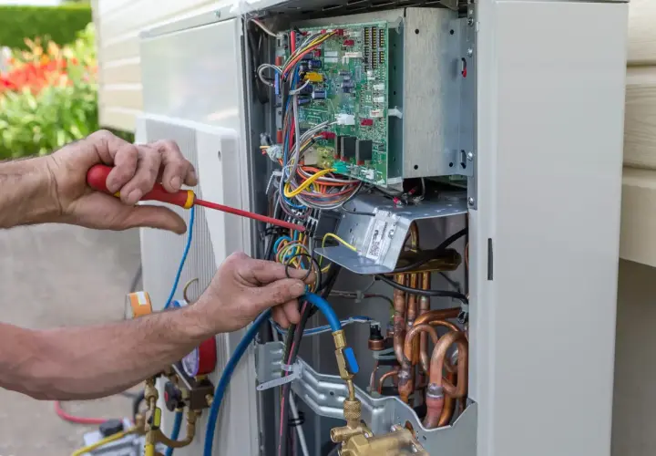 Fachowiec wykonuje serwis pomp ciepła Hitachi, pracując przy otwartej jednostce zewnętrznej z widoczną elektroniką i przewodami.
