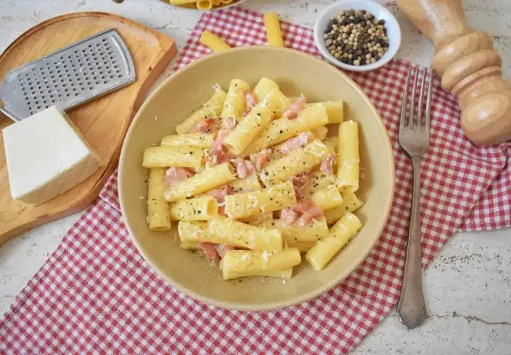 Pyszne pasta alla gricia z guanciale i pecorino, posypana świeżo mielonym pieprzem. Obok ser, tarka i młynek do pieprzu.