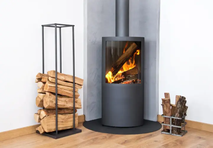 Moderner Kamin mit brennendem Holz. Ein Stapel Holz daneben. Diskussionen über ein holzheizung verbot sind angesichts dieser gemütlichen Szene unwahrscheinlich.