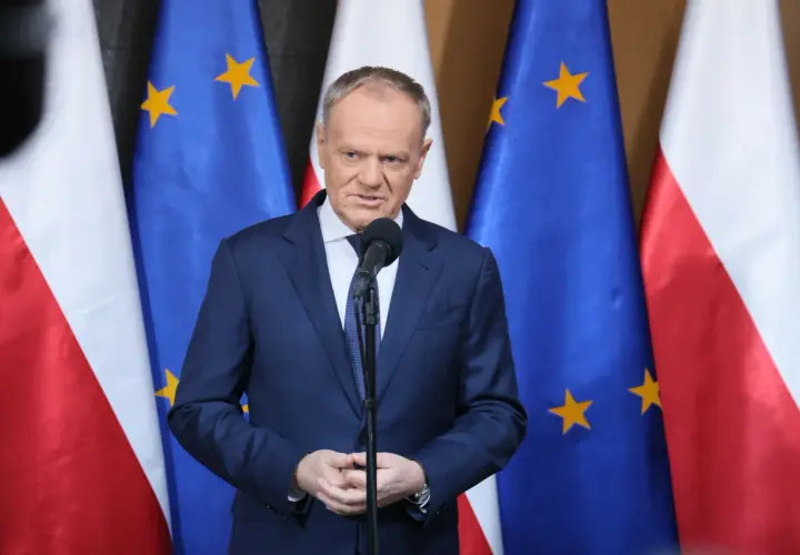 Premier przemawia na tle flag Polski i UE. Sondaże nie dają pewności, czy rząd koalicyjny przetrwa 2026 rok w niezmienionym składzie.