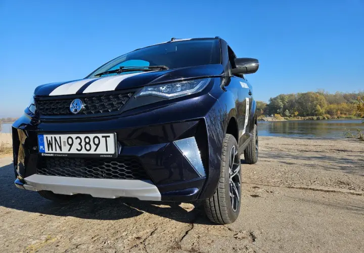 Ciemnoniebieskie aixam auto z białymi pasami na masce stoi nad rzeką w słoneczny dzień.