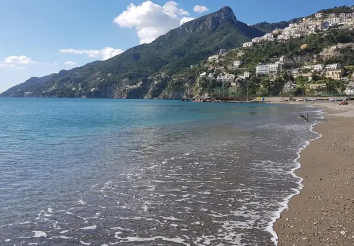 La plage de Vietri sul Mare s'étend sous un ciel bleu, avec des maisons blanches perchées sur la colline verdoyante. L'eau turquoise caresse le sable.