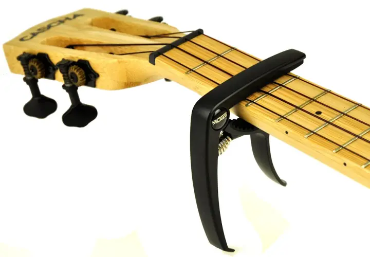 Czarny kapodaster do ukulele marki Moge na drewnianej podstrunnicy z widocznymi progami i strunami.