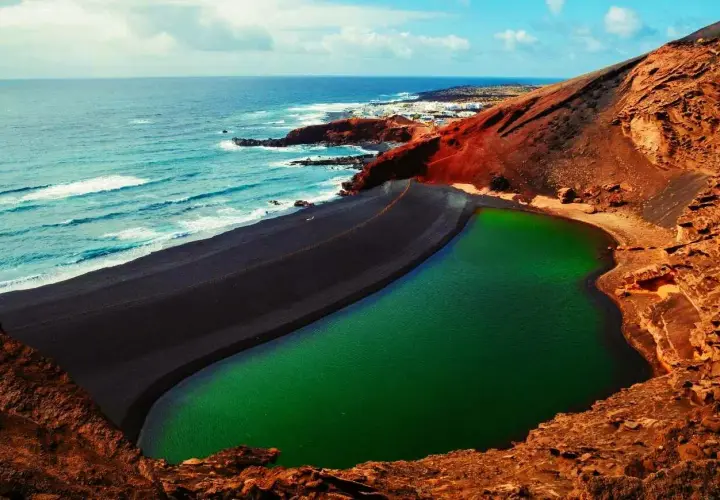 Zielona laguna otoczona czarną plażą i czerwonymi skałami. Niezwykłe miejsce, które warto zobaczyć na Lanzarote.