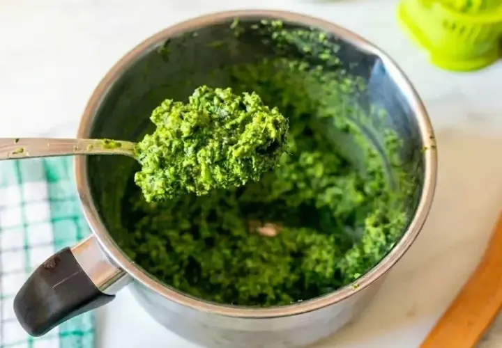 Łyżka świeżego, zielonego pesto bazyliowego nad metalowym garnkiem. Idealne do makaronu!