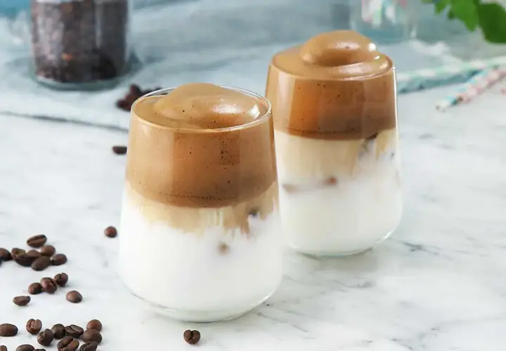 Två glas med krämigt iskaffe, perfekt för ett enkelt iskaffe recept. Kaffebönor sprider sig runt glasen.
