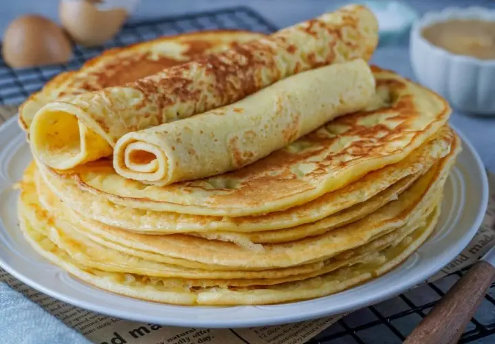 Ein Stapel goldbrauner Eierkuchen, zwei davon gerollt, warten auf ein leckeres Eierkuchen Rezept.
