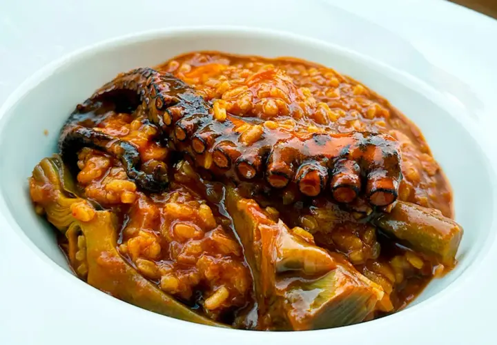 Delicioso arroz con pulpo y trozos de alcachofa en un cuenco blanco.