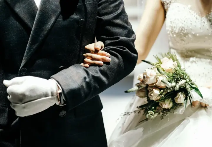 Ojciec prowadzi córkę do ołtarza, trzymając ją pod rękę. Panna młoda w białej sukni z bukietem różowych kwiatów.